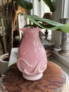 a pink vase sitting on top of a wooden table next to a green leafy plant