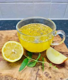 a glass cup filled with liquid next to an apple and sliced lemon on a cutting board