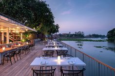 an outdoor dining area with tables and chairs overlooking the water at dusk, along with lit candles