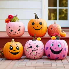 four pumpkins with faces painted on them are sitting on the front steps in front of a house