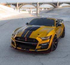 a yellow sports car with black stripes parked in front of a bridge