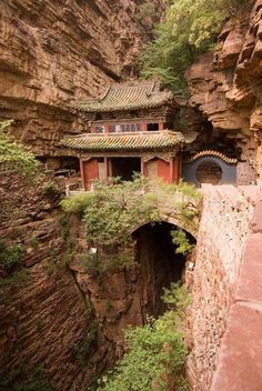 an old building is built into the side of a cliff in china, surrounded by greenery