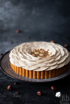 a cake with white frosting and nuts on a black plate next to some chocolate chips