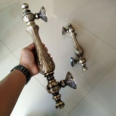 a person holding an ornate metal faucet in front of a white tiled floor