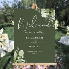 a welcome sign with flowers on it in front of a garden filled with white and green flowers