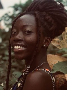 a woman with dreadlocks standing in front of some plants and smiling at the camera