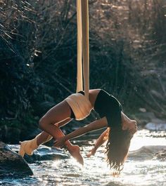 a woman hanging upside down from a pole in the middle of a river while holding onto her leg