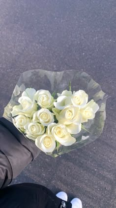 a person holding a bouquet of white roses in their hand on the street with no one around