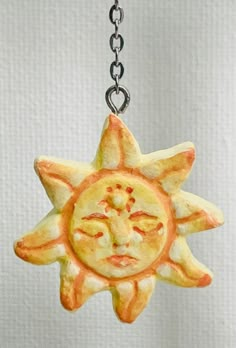 a ceramic sun ornament hanging from a chain on a white background with an orange and yellow design