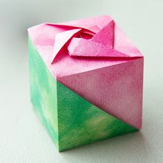 an origami box with a pink bow on the top and green paper inside