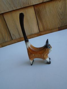 a cat figurine sitting on top of a white table next to a wooden fence