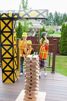 two children in safety vests and hard hats playing with wooden blocks on a deck