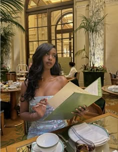 a woman in a dress is holding a piece of paper at a table with plates and silverware on it