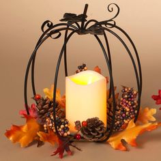 a lit candle sits in a pumpkin shaped holder with autumn leaves and pine cones around it