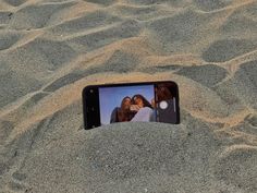 a cell phone laying in the sand with two women on it's screen, taken from above