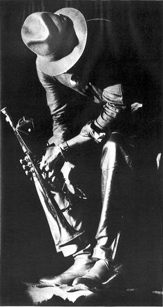 a black and white photo of a man with a hat on holding a musical instrument