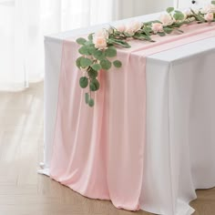 the table is decorated with pink flowers and greenery on it, along with white linens