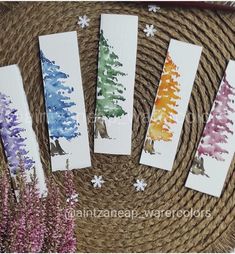 four watercolor trees are sitting on top of a wicker basket next to some flowers