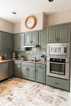 a kitchen with green cabinets and a large clock on the wall above the stove top