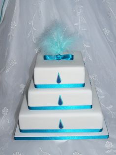 three tiered white cake with blue ribbon and feathers