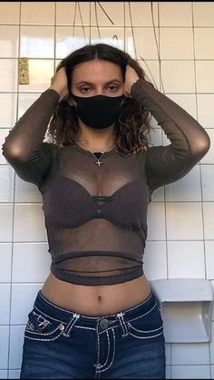 a woman wearing a black face mask standing in front of a white tiled wall