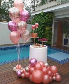 some pink and gold balloons are on the ground near a pool with a cake in it