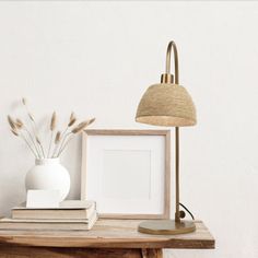 a white vase sitting on top of a wooden table next to a lamp and books