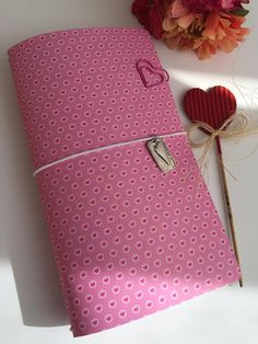 a pink dotted notebook with a heart on the cover and a flower bouquet in the background