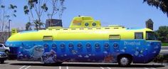 a yellow and blue submarine shaped bus parked in a parking lot next to a car