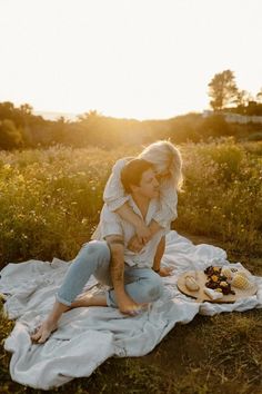 a woman sitting on top of a blanket next to a plate of food in a field