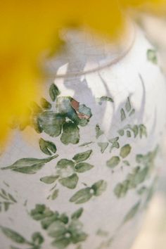 a close up view of a vase with flowers on it's side and yellow petals in the background