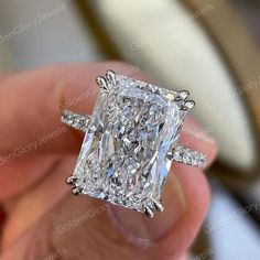 a person holding a fancy diamond ring in their hand, with the center stone surrounded by smaller diamonds