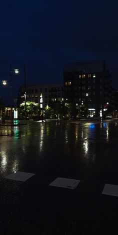 an empty parking lot at night with the lights on and buildings in the back ground