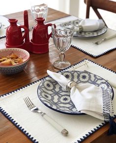 a dining table with place settings and dishes on it, ready to be set for dinner