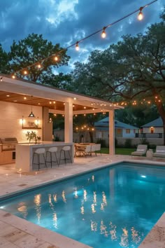 an outdoor kitchen and pool are lit up at night, with string lights strung across the pergolated area