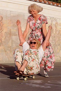 an older woman riding on top of a skateboard next to a younger man who is wearing sunglasses