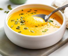 a white bowl filled with soup on top of a metal tray next to a spoon