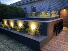 an outdoor hot tub lit up at night with plants growing on the wall and below it