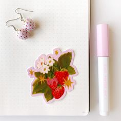 a strawberry and flower sticker next to a pen on top of a notepad