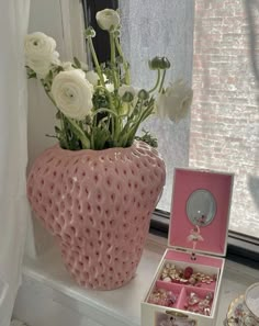 a pink vase filled with white flowers next to a window sill and jewelry box