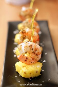 shrimp and pineapple appetizer on a black plate with toothpicks in the middle