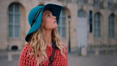 a woman wearing a blue hat looking up at something in front of an old building