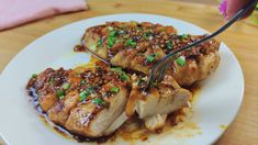 two pieces of meat on a white plate with sauce and green onions being drizzled over it