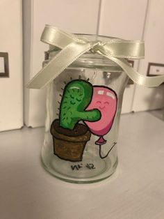 a glass jar with a cactus painted on the side and a ribbon tied around it