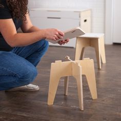 a woman sitting on the floor next to a small wooden stool with a book in it