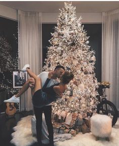 a man and woman kissing in front of a white christmas tree with presents on the floor