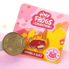 a coin sitting on top of a pink card next to a pin with an image of a frog