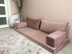 a pink couch sitting on top of a white rug next to a vase with flowers