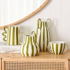 three green and white striped vases sitting on top of a wooden table next to a stack of books