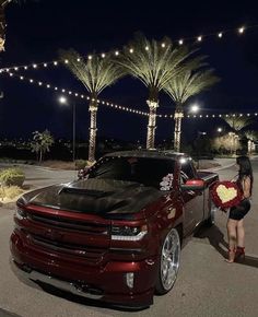 a woman standing next to a red car with flowers in front of it at night